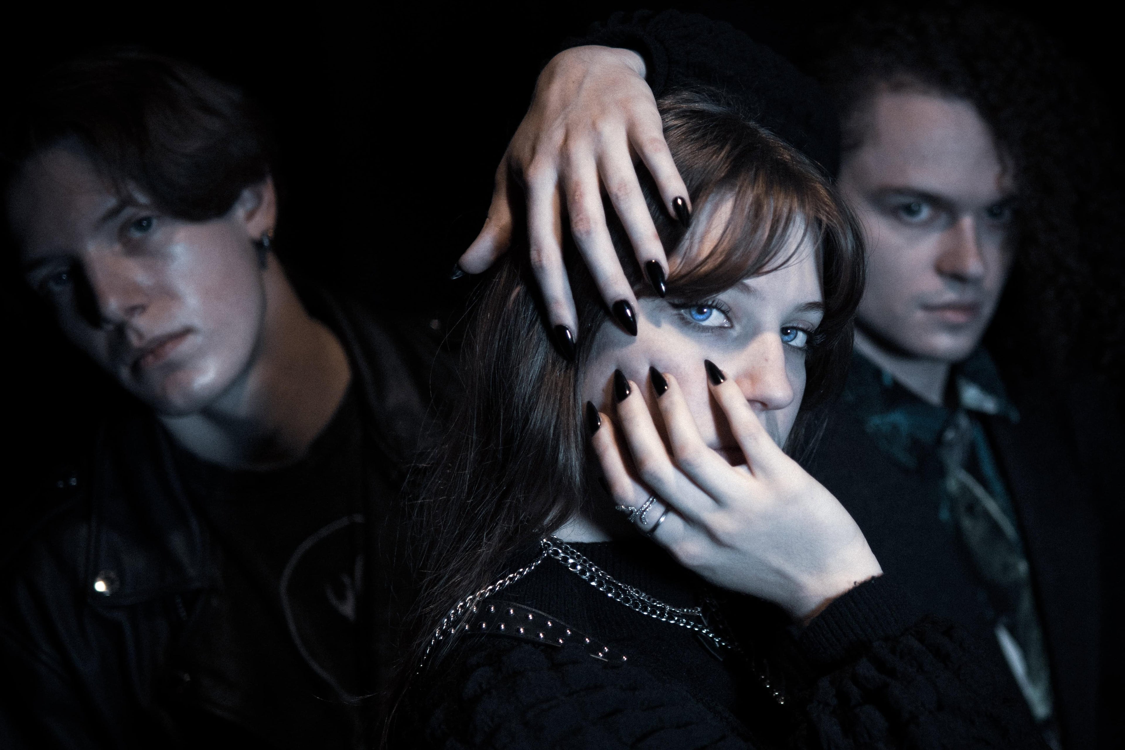 Three people with a central figure holding their face, against a dark background
