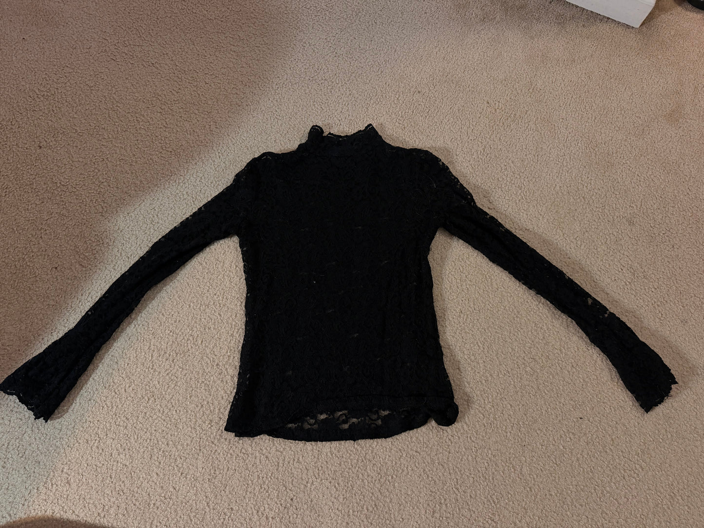 A black long-sleeve knit top laid flat on a beige carpeted floor.