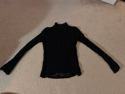 A black long-sleeve knit top laid flat on a beige carpeted floor.